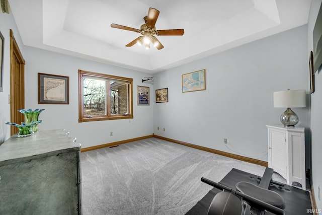 interior space featuring baseboards, a raised ceiling, light carpet, and ceiling fan