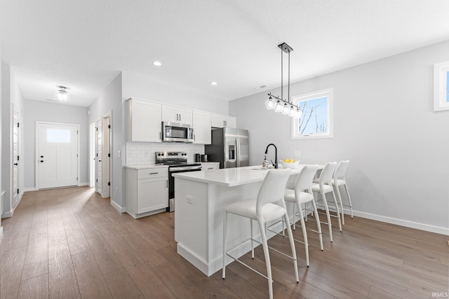 kitchen with appliances with stainless steel finishes, decorative backsplash, light wood finished floors, and a kitchen bar