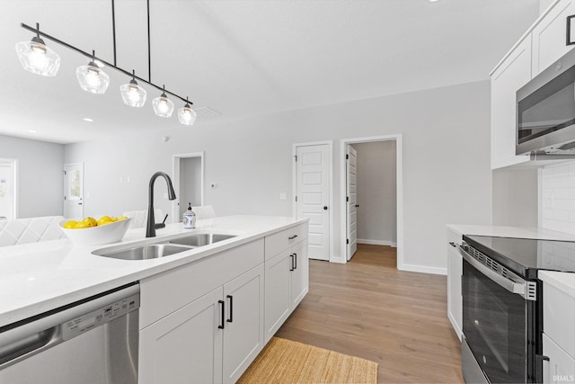 kitchen featuring stainless steel appliances, a sink, white cabinets, light countertops, and light wood-type flooring