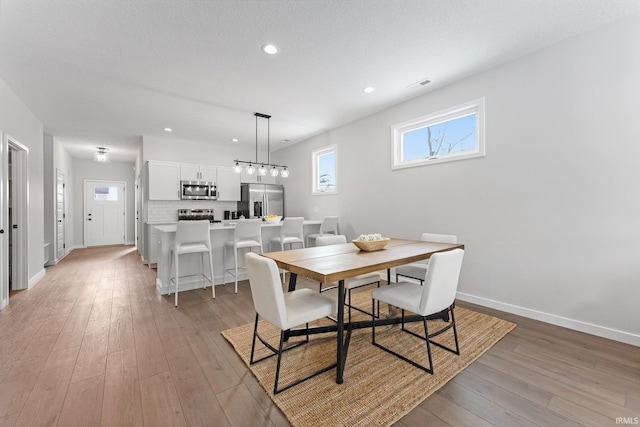 dining space featuring recessed lighting, visible vents, light wood-style flooring, a textured ceiling, and baseboards