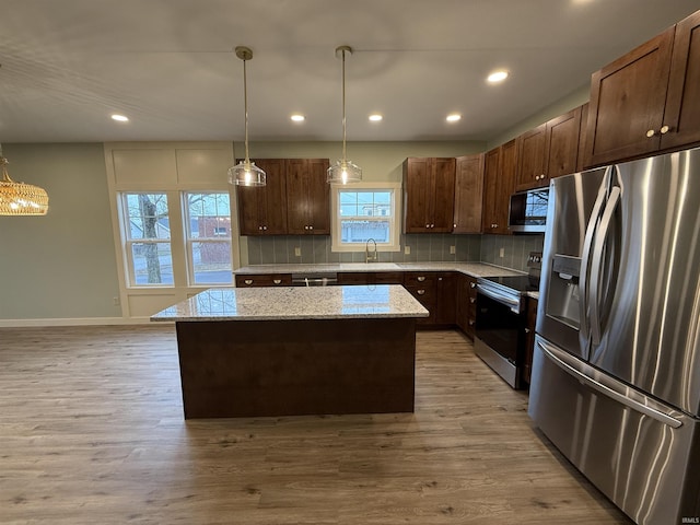 kitchen with light wood finished floors, a kitchen island, stainless steel appliances, and a sink