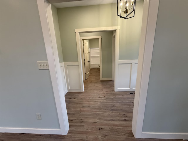 corridor with a wainscoted wall, a notable chandelier, wood finished floors, and a decorative wall