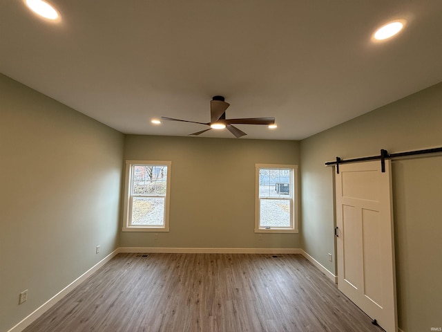 unfurnished bedroom featuring a barn door, baseboards, ceiling fan, and wood finished floors