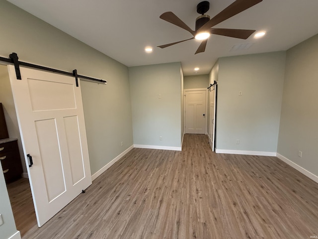 spare room with baseboards, a barn door, a ceiling fan, and wood finished floors