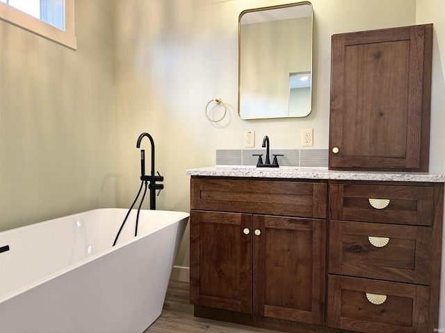 full bath with a freestanding tub, wood finished floors, and vanity