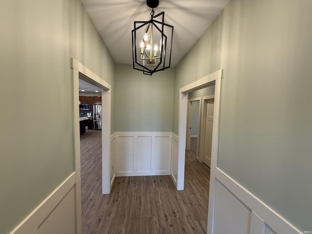 hall featuring wainscoting, an inviting chandelier, wood finished floors, and a decorative wall