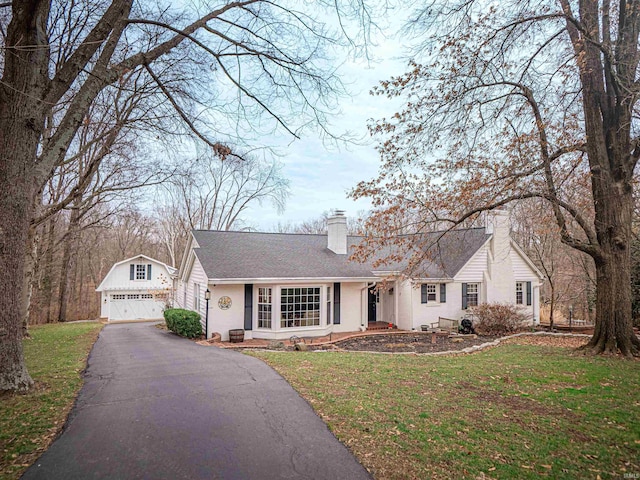 view of front of property with a front lawn, roof with shingles, a chimney, a garage, and an outbuilding