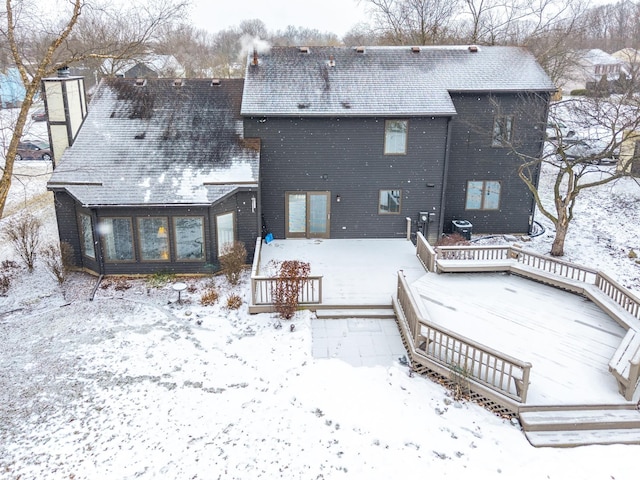 snow covered back of property with a chimney, a deck, and brick siding