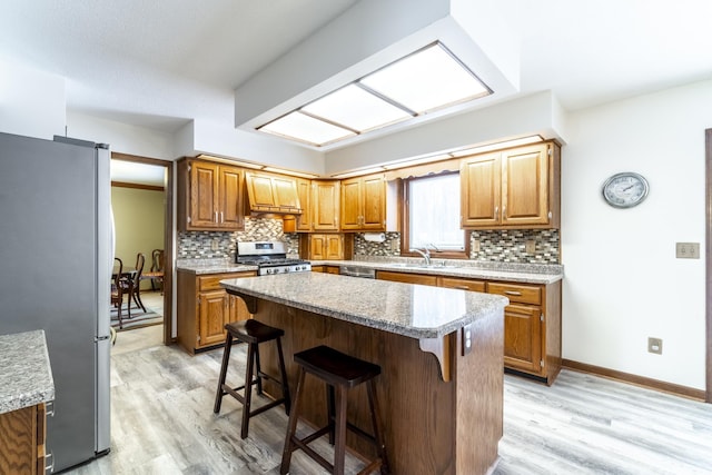 kitchen featuring custom range hood, a breakfast bar, stainless steel appliances, light wood-style floors, and a sink