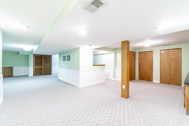 finished basement featuring wainscoting, visible vents, and light colored carpet