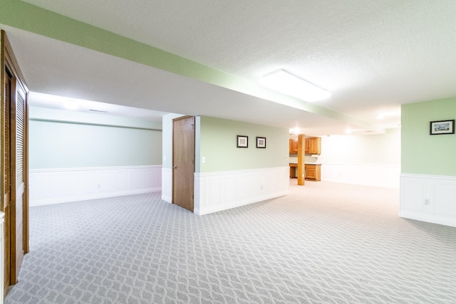 finished below grade area with wainscoting, light carpet, and a textured ceiling