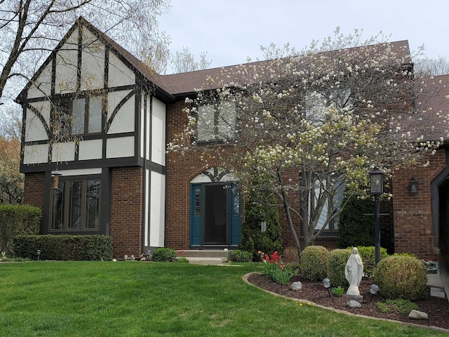 tudor house featuring stucco siding, a shingled roof, brick siding, and a front yard