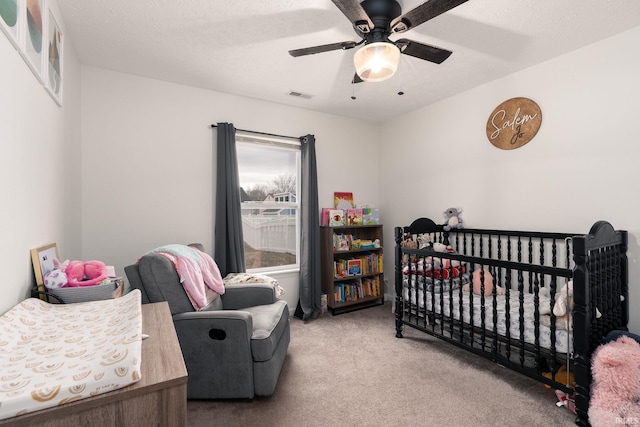 carpeted bedroom featuring a nursery area, ceiling fan, visible vents, and a textured ceiling