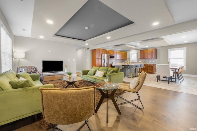 living area featuring visible vents, baseboards, a raised ceiling, light wood-style flooring, and recessed lighting