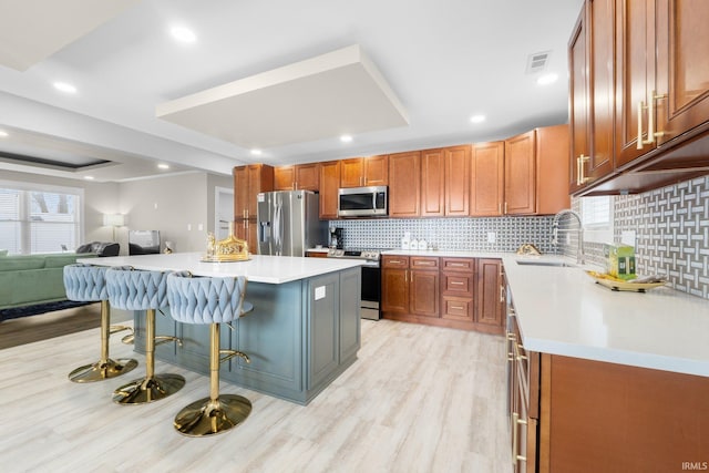 kitchen featuring light wood finished floors, a kitchen breakfast bar, a tray ceiling, stainless steel appliances, and a sink