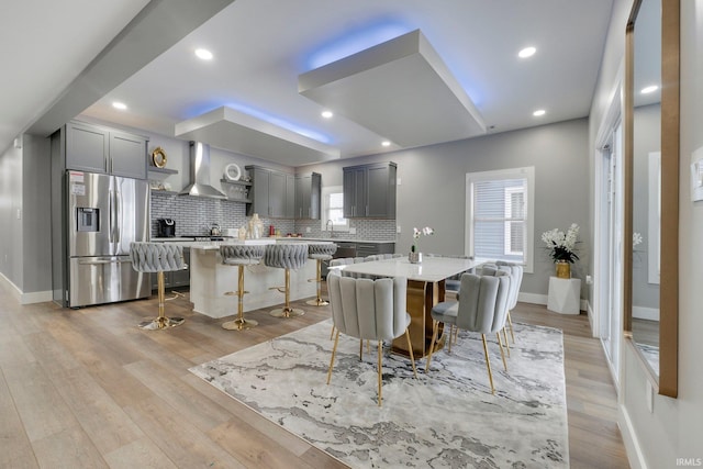 kitchen featuring wall chimney range hood, gray cabinets, decorative backsplash, and stainless steel fridge with ice dispenser