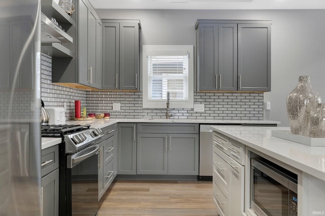 kitchen featuring tasteful backsplash, appliances with stainless steel finishes, gray cabinetry, light wood-type flooring, and a sink