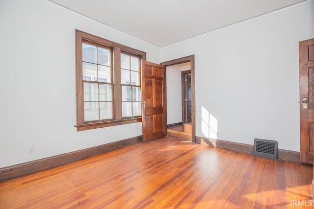 spare room featuring wood finished floors, visible vents, and baseboards