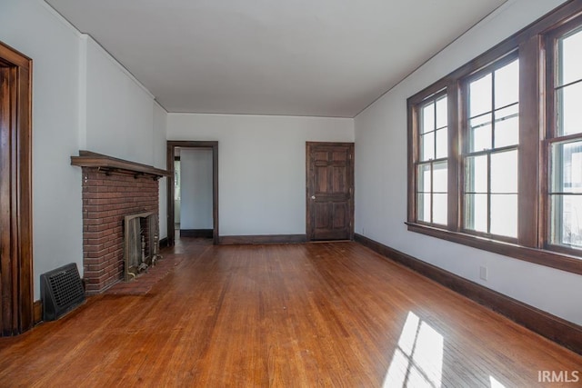 unfurnished living room featuring a brick fireplace, baseboards, and wood finished floors