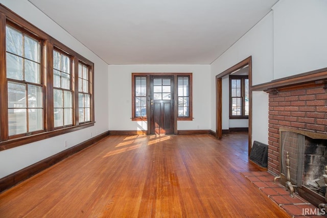 unfurnished living room with plenty of natural light, a fireplace, baseboards, and wood finished floors