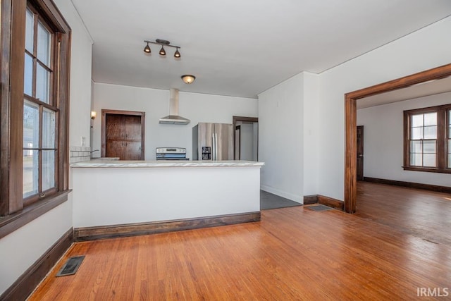 interior space with stainless steel appliances, visible vents, wall chimney range hood, wood finished floors, and baseboards