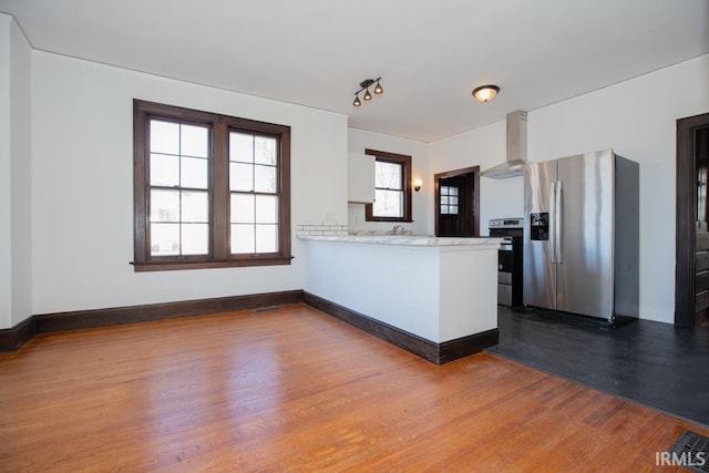 kitchen with dark wood-style floors, appliances with stainless steel finishes, a peninsula, light countertops, and wall chimney range hood