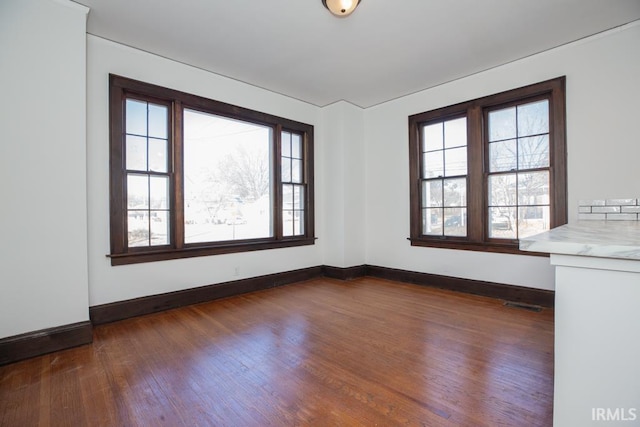 unfurnished room featuring dark wood finished floors, visible vents, and baseboards