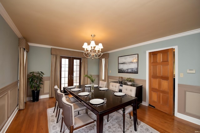 dining room with french doors, crown molding, wainscoting, wood finished floors, and a chandelier