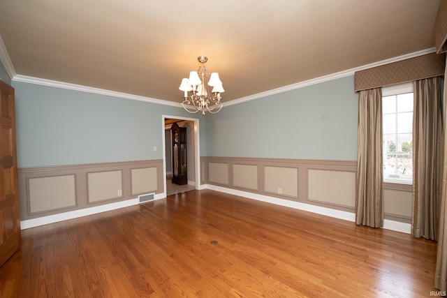 empty room with wainscoting, wood finished floors, visible vents, and an inviting chandelier