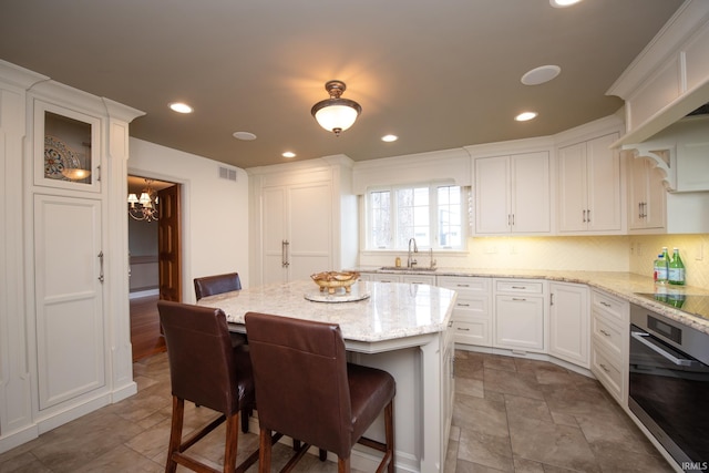 kitchen featuring a center island, white cabinetry, stainless steel oven, a sink, and a kitchen bar