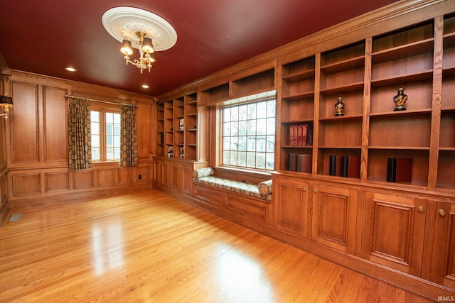 empty room with a chandelier, light wood finished floors, visible vents, and a healthy amount of sunlight