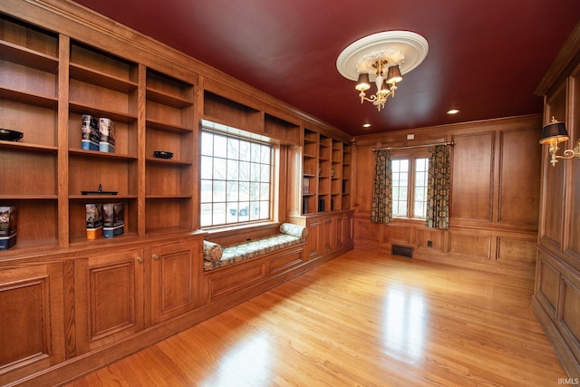 spare room featuring crown molding, visible vents, a decorative wall, an inviting chandelier, and light wood-type flooring