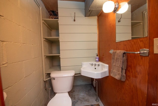 half bathroom featuring concrete block wall, toilet, a sink, wooden walls, and concrete flooring