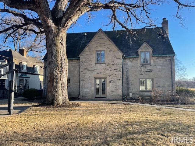 view of front facade featuring stone siding, a chimney, a front lawn, and french doors