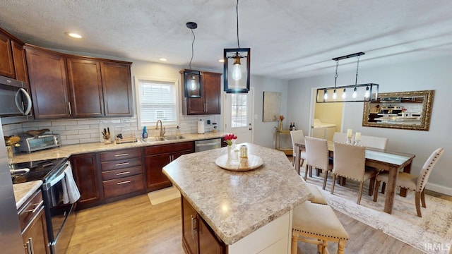 kitchen featuring stainless steel appliances, a kitchen island, a sink, light wood-style floors, and backsplash