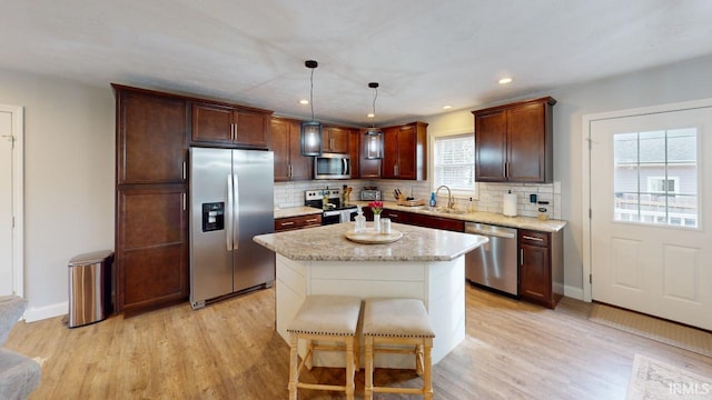 kitchen featuring light wood finished floors, decorative backsplash, stainless steel appliances, and a sink