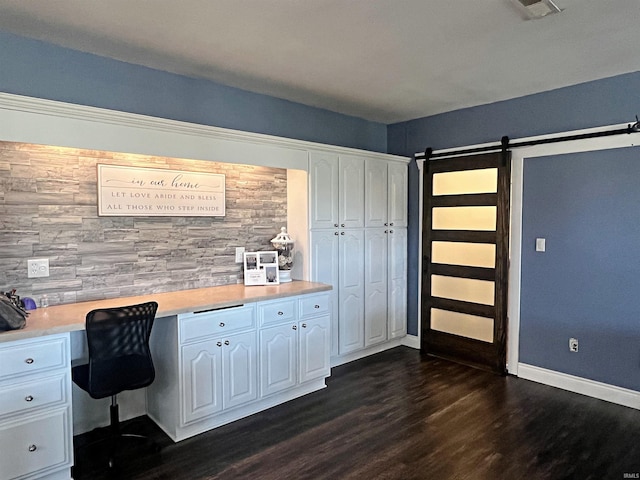 unfurnished office featuring a barn door, visible vents, dark wood finished floors, baseboards, and built in study area