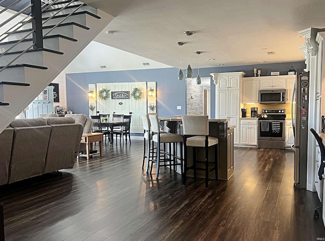 kitchen featuring dark wood-style floors, open floor plan, stainless steel appliances, a kitchen bar, and pendant lighting