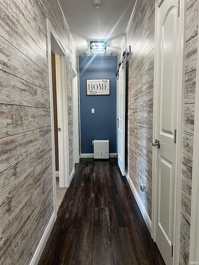 corridor featuring a barn door, wooden walls, a textured ceiling, wood finished floors, and baseboards