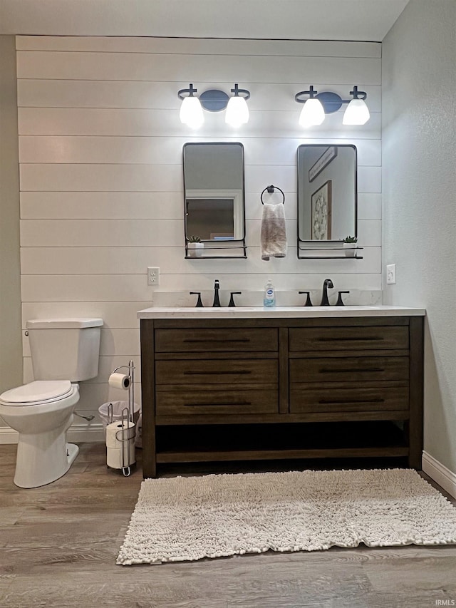 bathroom with double vanity, toilet, a sink, wood finished floors, and baseboards