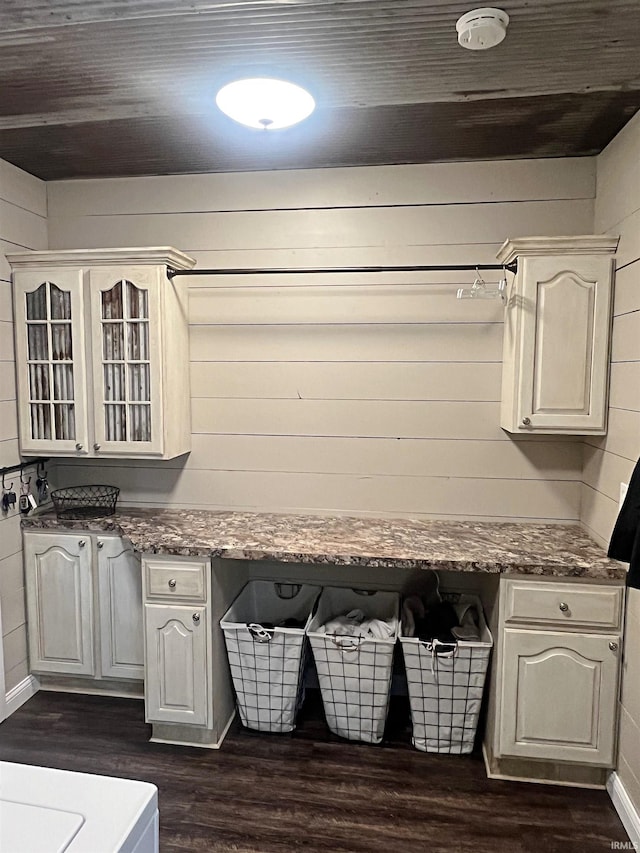 kitchen featuring dark wood-type flooring, glass insert cabinets, built in study area, wood walls, and a peninsula