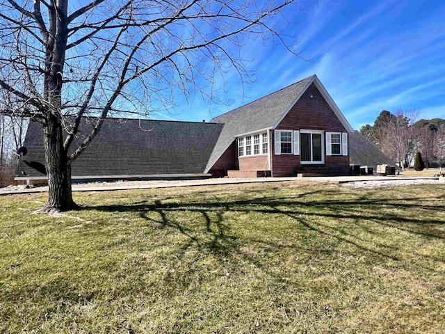 view of front facade with brick siding, a front yard, and a shingled roof