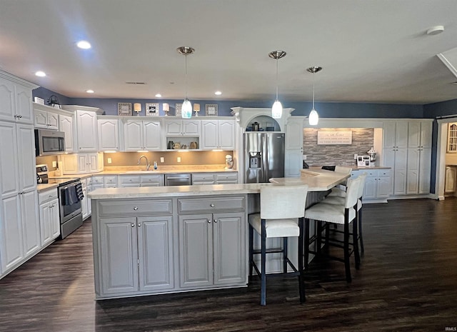 kitchen with dark wood-style floors, stainless steel appliances, a spacious island, light countertops, and white cabinets