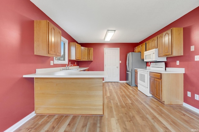 kitchen featuring white appliances, a peninsula, light countertops, light wood-style floors, and a sink