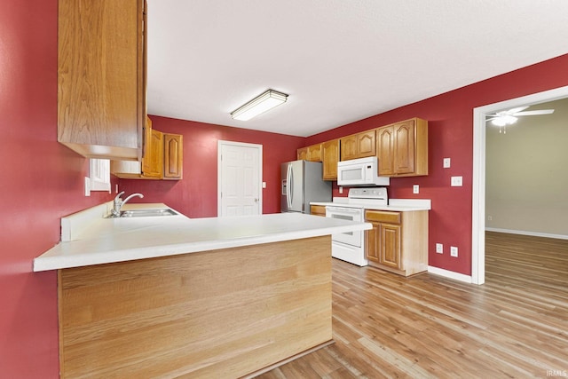 kitchen with a peninsula, white appliances, a sink, baseboards, and light wood-style floors