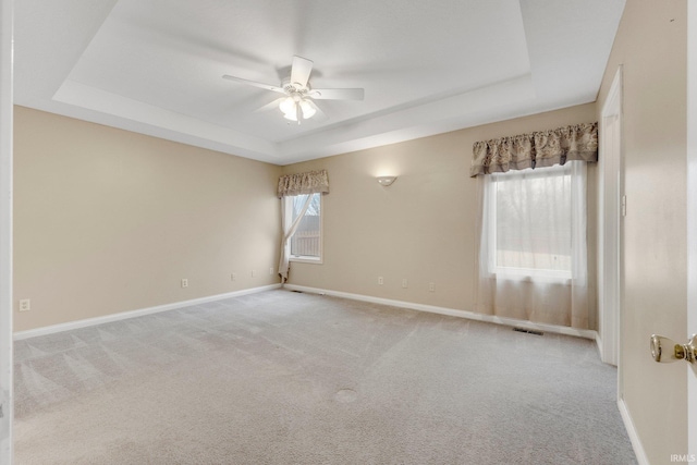 carpeted empty room featuring a raised ceiling, visible vents, ceiling fan, and baseboards