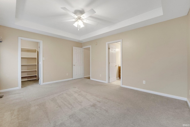 unfurnished bedroom featuring a tray ceiling, light carpet, a spacious closet, and baseboards