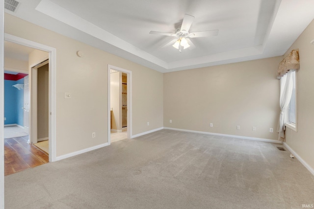 empty room with a raised ceiling, visible vents, and baseboards