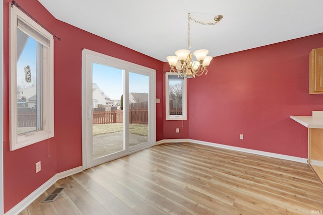 unfurnished dining area with a chandelier, light wood-style flooring, visible vents, and baseboards