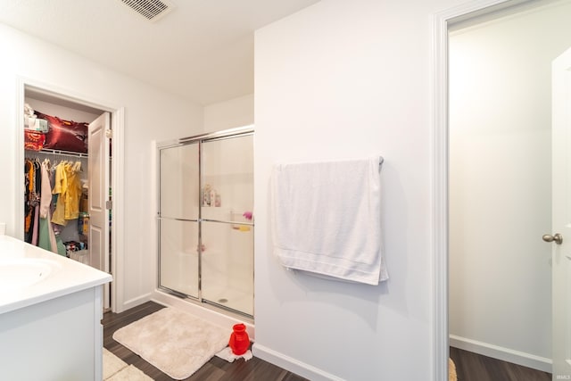 full bathroom with a stall shower, a spacious closet, visible vents, and wood finished floors